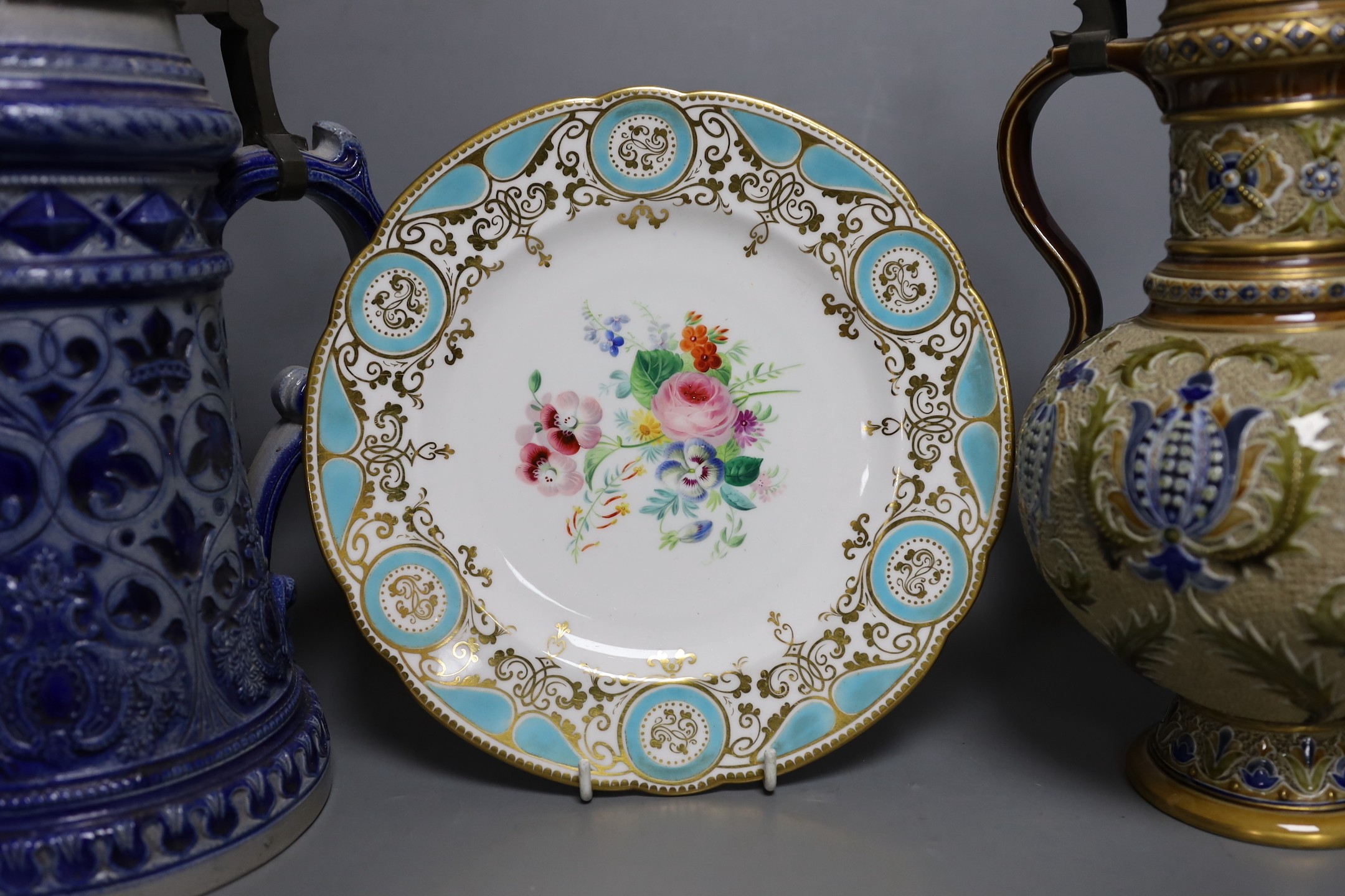 A Mettlach stoneware stein, 29.5 cm high, a German blue stoneware stein, a Staffordshire porcelain cottage pastille burner and an English porcelain floral plate